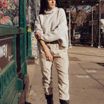 Female model is standing on a foot path wearing a textured cream knitted jersey, bone coloured corduroy tapered trousers and chunky black boots