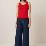 A female model wears a classic red singlet with a simple, sleeveless design, ideal for layering or wearing solo.Worn here with wide leg dark blue jeans and tan ballet flats