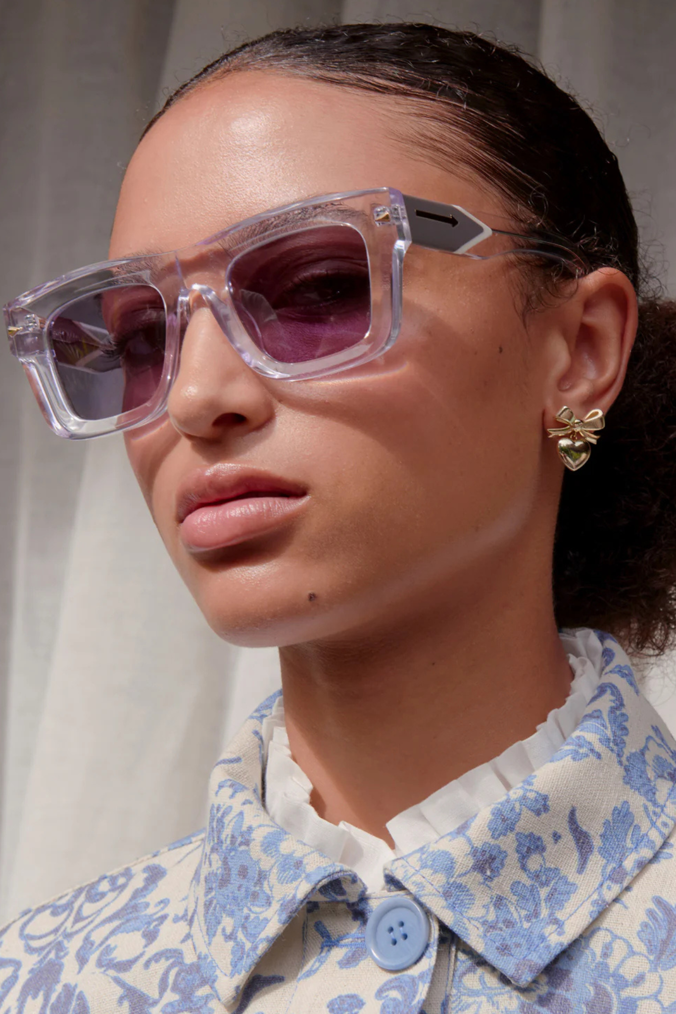 Close up of a woman face wearing  the Karen Walker deep space sunglasses. A bold clear square framed style with a purple black lense.